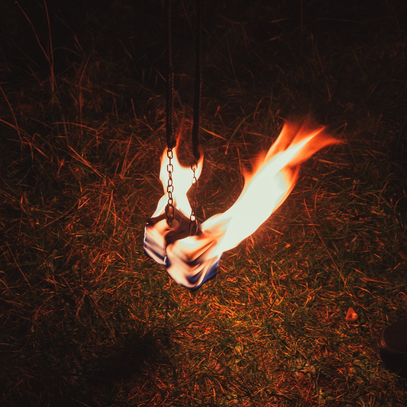 a closeup shot of fire poi lit, hanging in front of grass