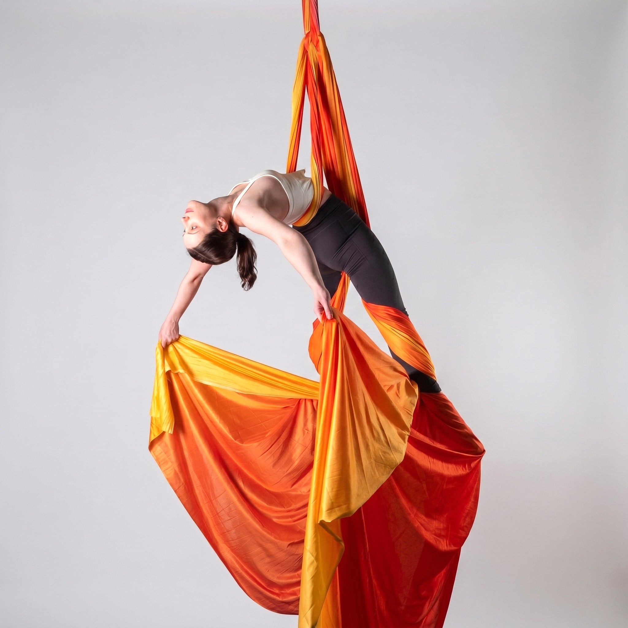 Person performing aerial acrobatics with orange and red fabric against a plain background