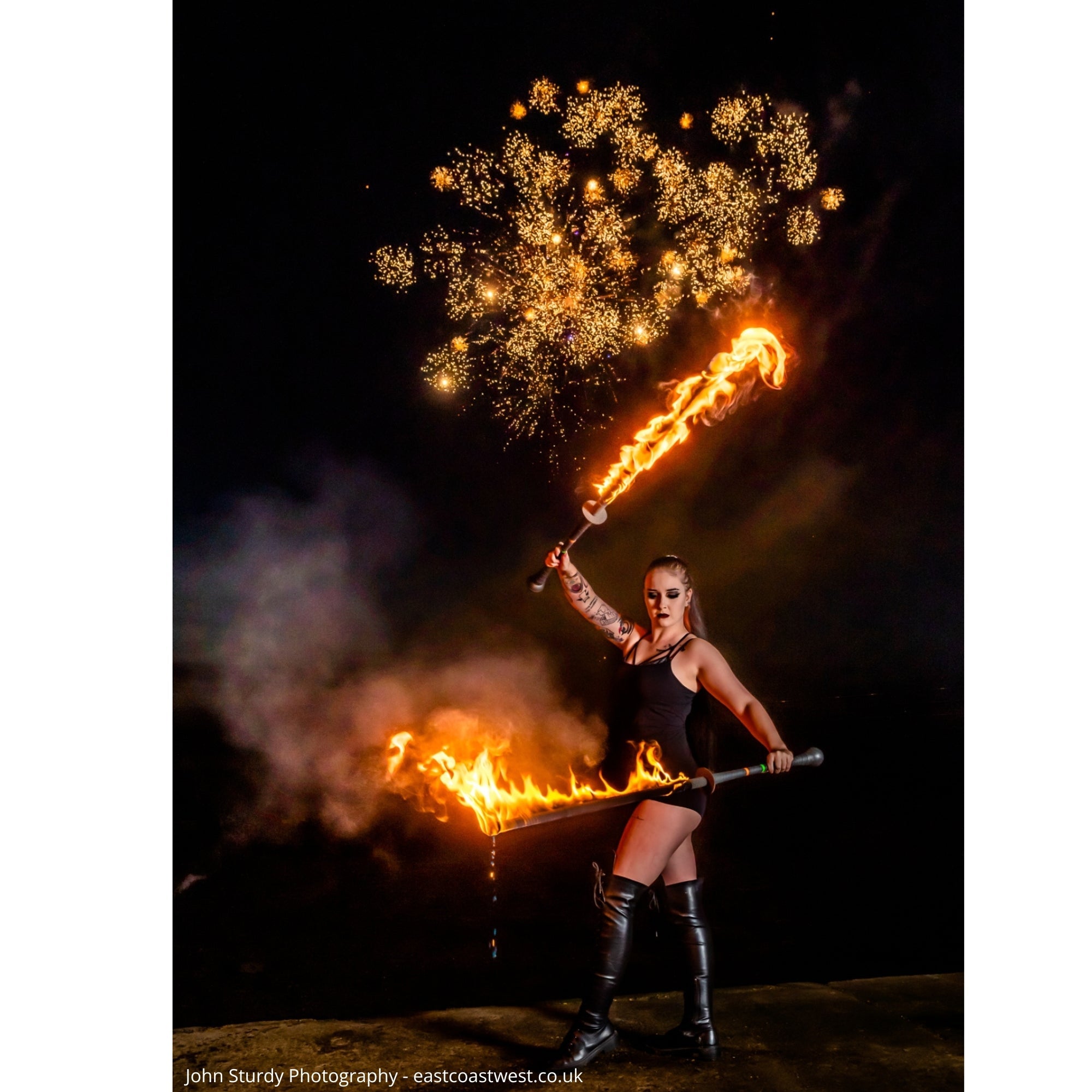 performer with two swords on fire and fireworks in the background